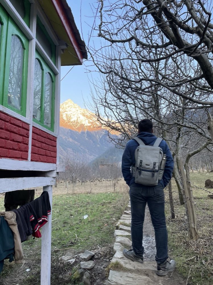 Sunset lighting a snow peak behind a traditional Himachali house in Kasol